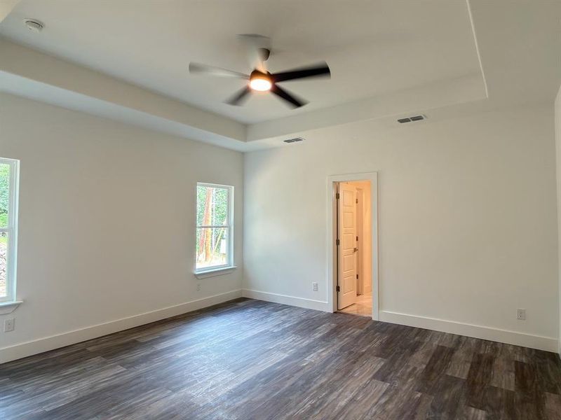 Spacious room featuring wood-finish flooring, a contemporary ceiling fan with integrated lighting, and a tray ceiling detail