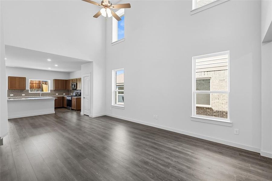 Unfurnished living room featuring a towering ceiling, dark wood finished floors, and a ceiling fan Unfurnished living room featuring a towering ceiling, dark wood finished floors, and a ceiling fan