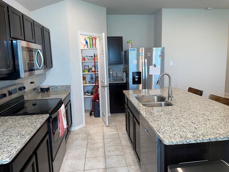 Kitchen featuring appliances with stainless steel finishes, light stone countertops, a kitchen bar, and a kitchen island with sink