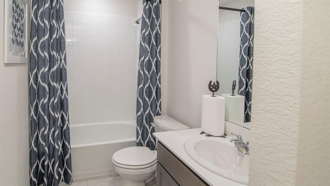 Bathroom featuring a textured wall, vanity, shower / tub combo with curtain, and light tile patterned flooring