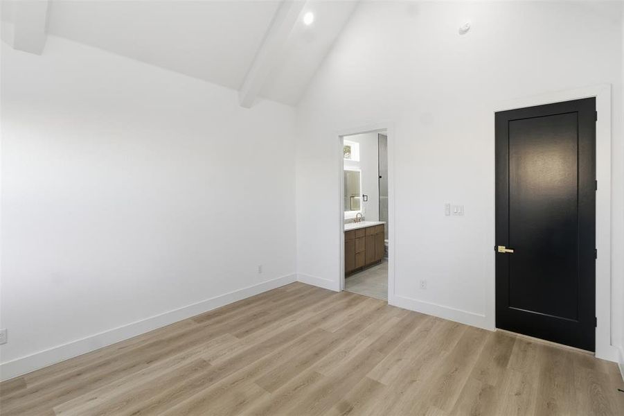 Unfurnished bedroom featuring light wood finished floors, ensuite bath, lofted ceiling, and recessed lighting