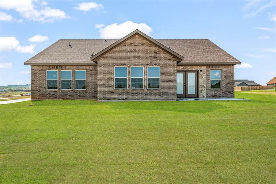 Rear view of property with a shingled roof, brick siding, a lawn, and french doors