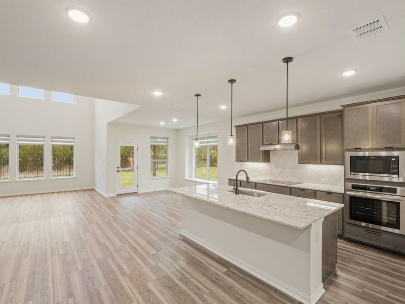 Kitchen featuring light stone counters, stainless steel appliances, a center island with sink, tasteful backsplash, and pendant lighting