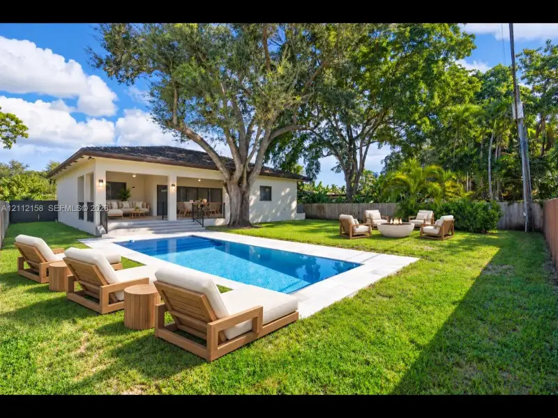 Resort-style backyard with an in-ground pool, stone paver deck, covered patio, and mature trees for natural shade and privacy