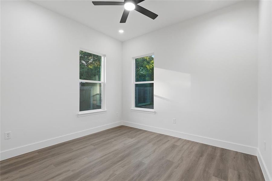 Room featuring wood-finish flooring, white walls, and two windows