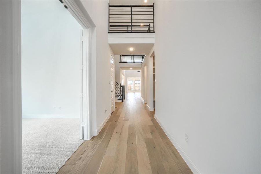 Hall with stairway, baseboards, light wood-style floors, and a towering ceiling