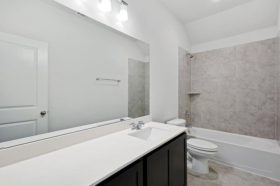 Full bathroom with tile patterned flooring, toilet, lofted ceiling, tiled shower / bath combo, and vanity