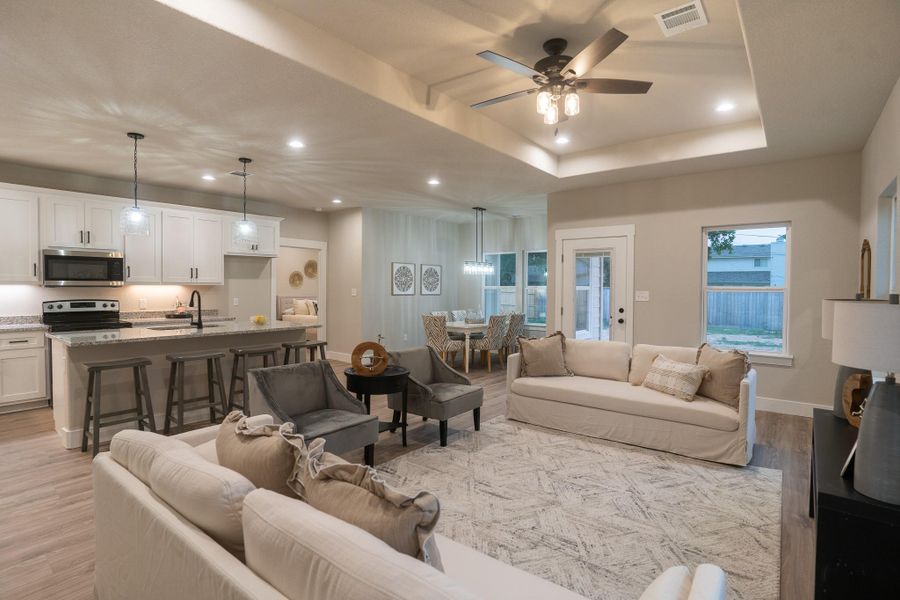 Living area featuring light wood finished floors, recessed lighting, ceiling fan, a raised ceiling, and baseboards