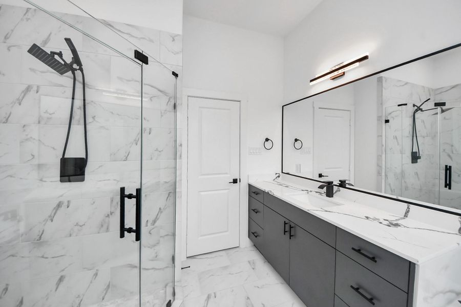 This bathroom features a sleek, modern design with a spacious glass-enclosed shower, dual vanities with quartz countertops, and stylish black fixtures, all set against elegant marble tile. This bathroom features a sleek, modern design with a spacious glass-enclosed shower, dual vanities with quartz countertops, and stylish black fixtures, all set against elegant marble tile.