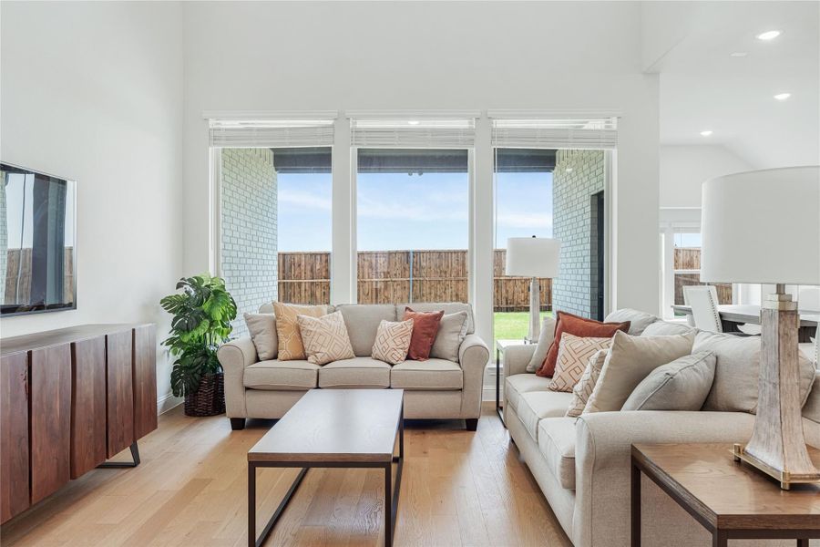 Living room with two beige sofas, hardwood floors, and large windows overlooking a backyard