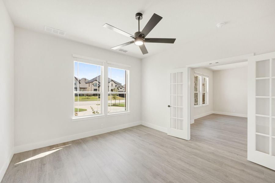 Empty room with light wood floors, ceiling fan, white walls, and French doors
