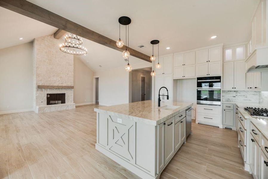 Kitchen featuring light stone counters, backsplash, white cabinetry, light wood-style flooring, and decorative light fixtures Kitchen featuring light stone counters, backsplash, white cabinetry, light wood-style flooring, and decorative light fixtures