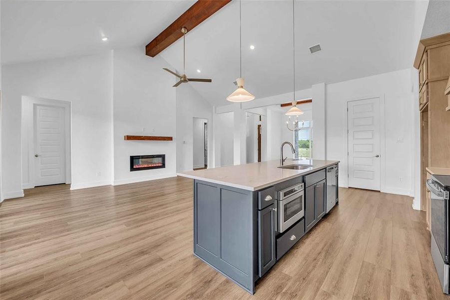 Kitchen with a sink, light countertops, a glass covered fireplace, light wood-style flooring, and beamed ceiling Kitchen with a sink, light countertops, a glass covered fireplace, light wood-style flooring, and beamed ceiling