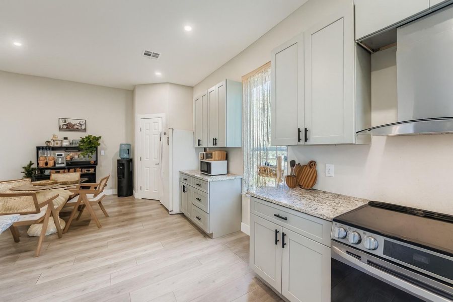 Kitchen with white appliances, wall chimney exhaust hood, light wood-style flooring, light stone counters, and recessed lighting Kitchen with white appliances, wall chimney exhaust hood, light wood-style flooring, light stone counters, and recessed lighting