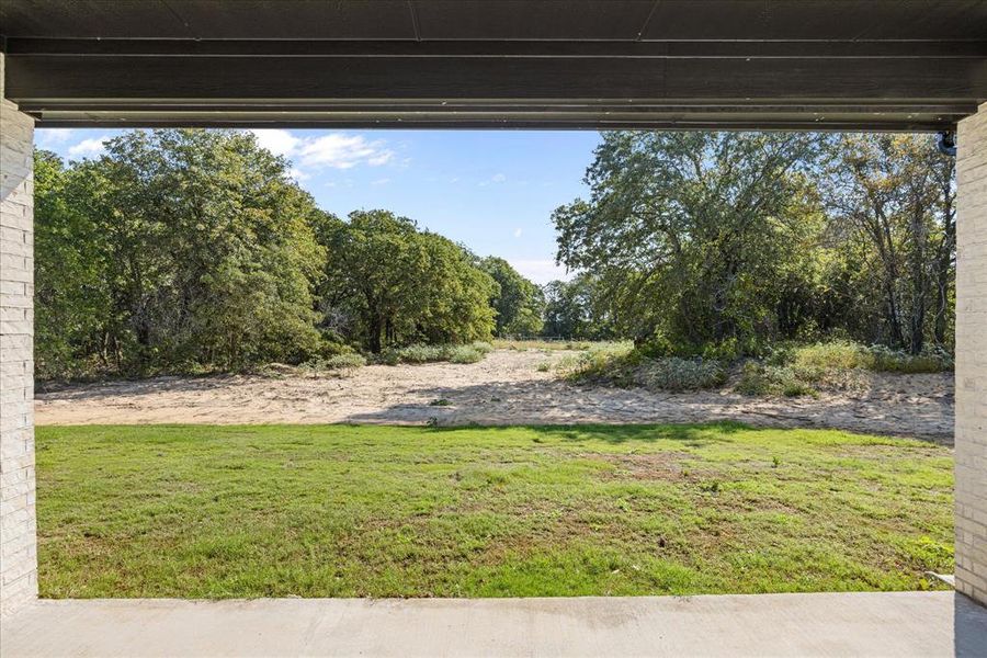Covered patio overlooking a spacious backyard with established trees.