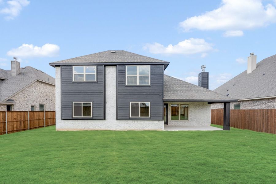Two-story home rear exterior with dark siding, brick accents, covered patio, and fenced backyard with green lawn