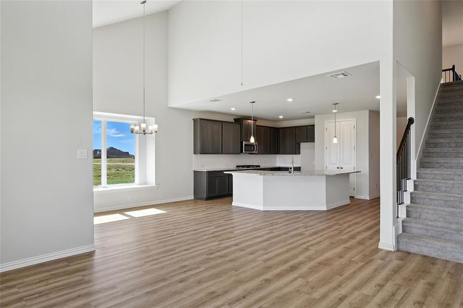 Kitchen with a towering ceiling, stainless steel microwave, light wood finished floors, an island with sink, and dark brown cabinets Kitchen with a towering ceiling, stainless steel microwave, light wood finished floors, an island with sink, and dark brown cabinets