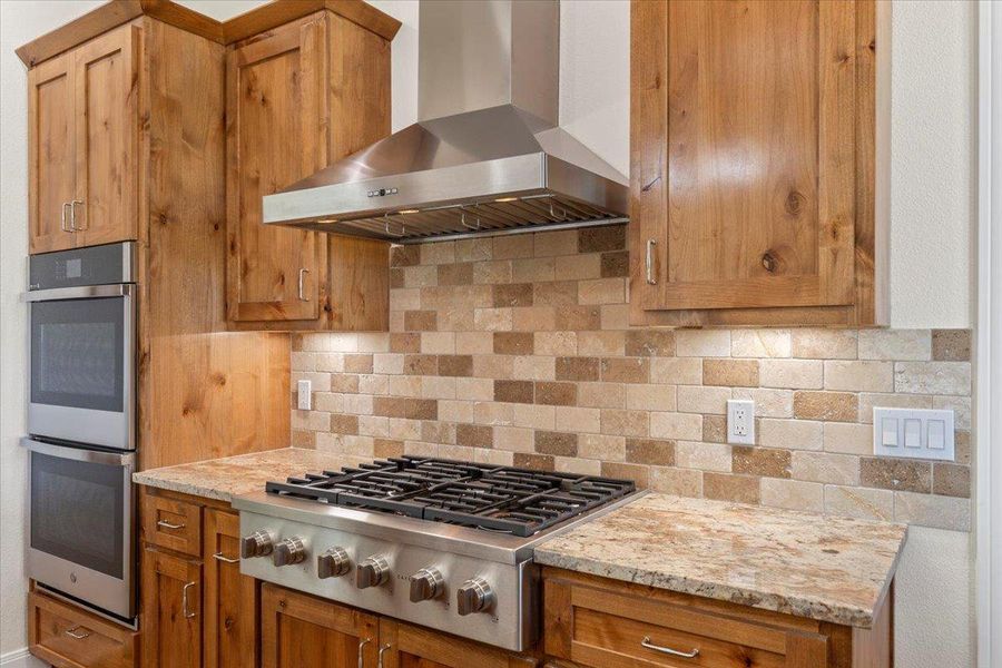 Kitchen with wall chimney exhaust hood, stainless steel appliances, decorative backsplash, and brown cabinets