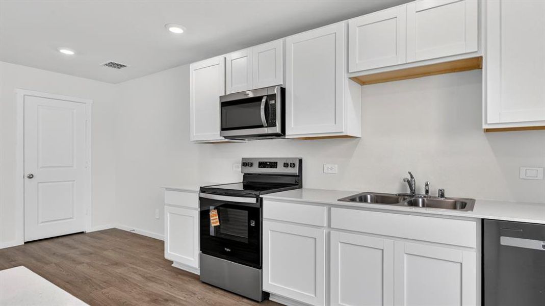 Kitchen featuring white shaker-style cabinetry, stainless steel appliances, light-toned countertops, and wood-finish flooring
