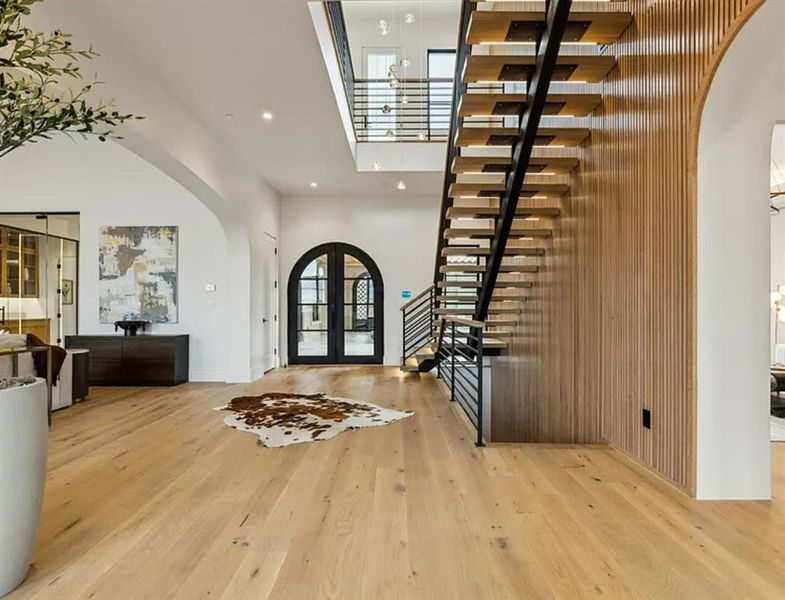 Entrance foyer with arched walkways, french doors, light wood-style flooring, recessed lighting, and a high ceiling