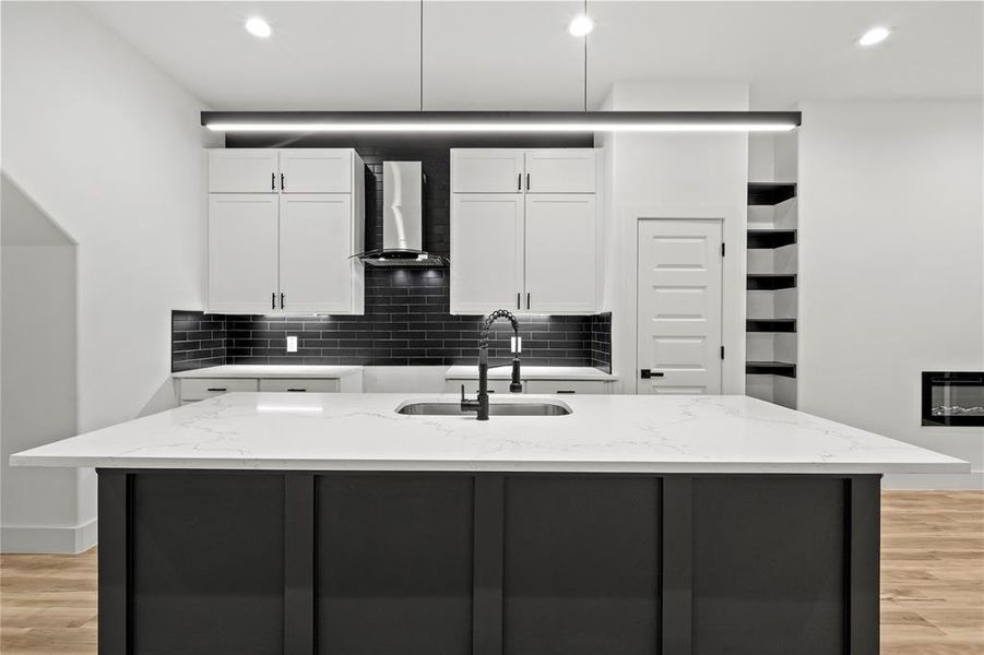 Kitchen with ceiling fan, hanging light fixtures, wall chimney range hood, a kitchen island with sink, and white cabinets