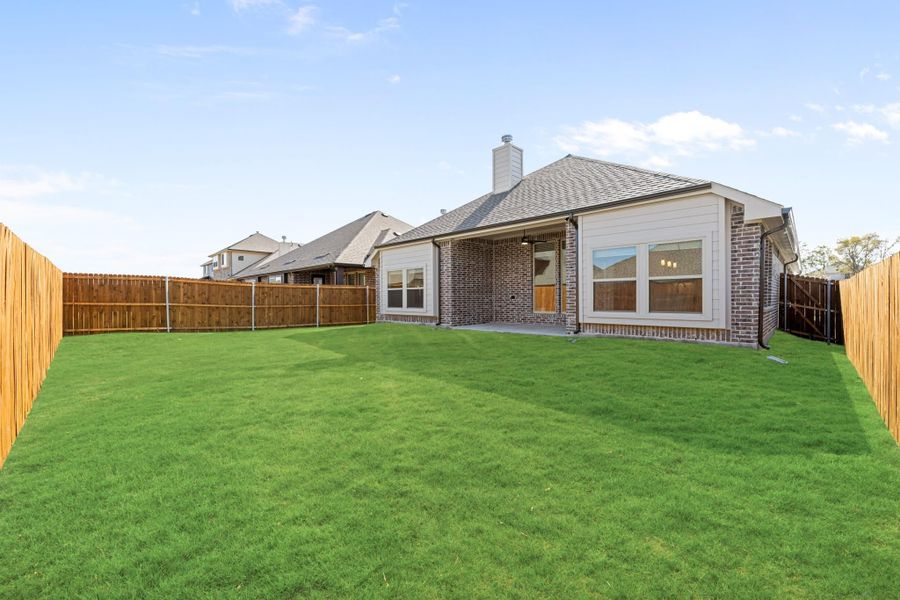Backyard of brick home with covered patio, large green lawn, and wood privacy fence on both sides. Backyard of brick home with covered patio, large green lawn, and wood privacy fence on both sides.