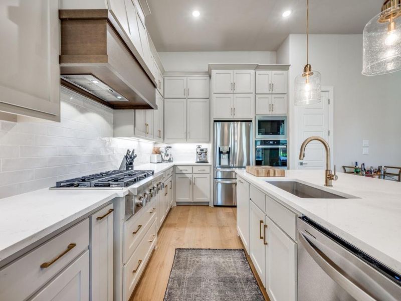 Kitchen featuring stainless steel appliances, a sink, custom range hood, pendant lighting, and white cabinetry
