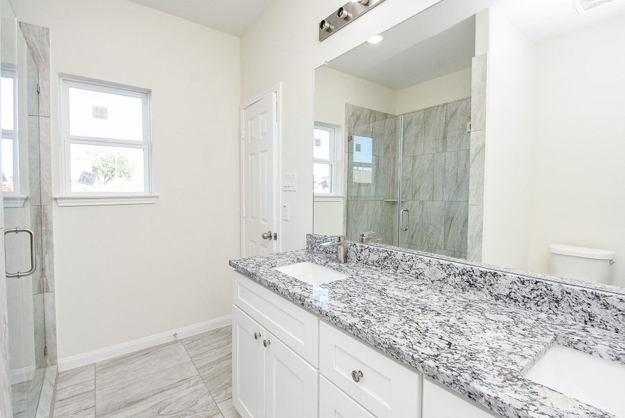 Modern bathroom with dual vanity, granite countertops, large mirror, tiled shower, and neutral color palette.