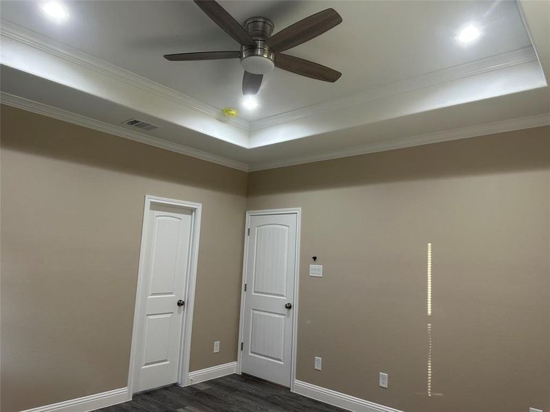 Spare room with a tray ceiling, dark wood-style flooring, crown molding, baseboards, and ceiling fan