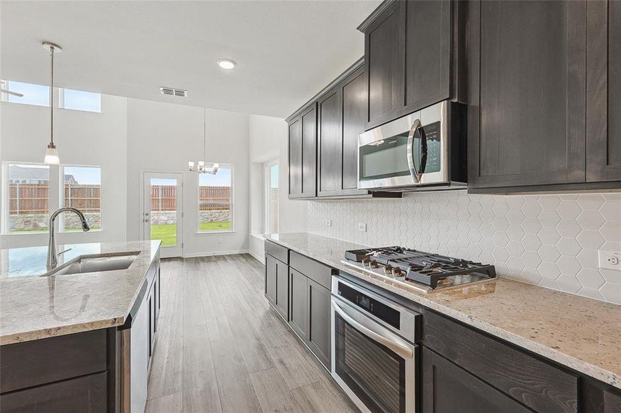 Kitchen with decorative backsplash, stainless steel appliances, hanging light fixtures, and sink