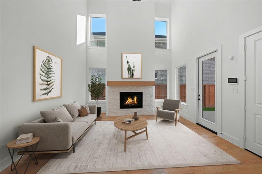Living room featuring a high ceiling, a warm lit fireplace, and wood finished floors Living room featuring a high ceiling, a warm lit fireplace, and wood finished floors