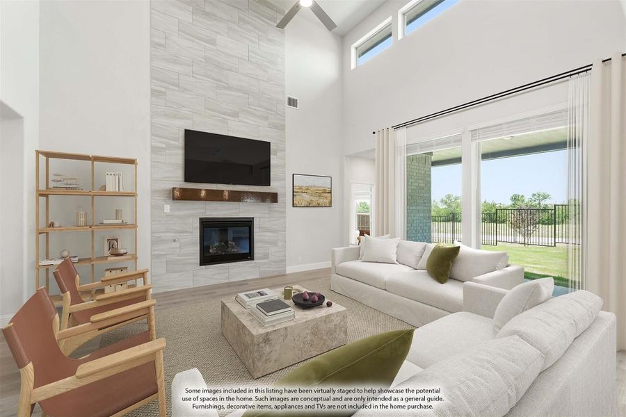 Living room with two-story tile fireplace wall, ceiling fan, white sofas, and large windows overlooking a backyard patio. Living room with two-story tile fireplace wall, ceiling fan, white sofas, and large windows overlooking a backyard patio.