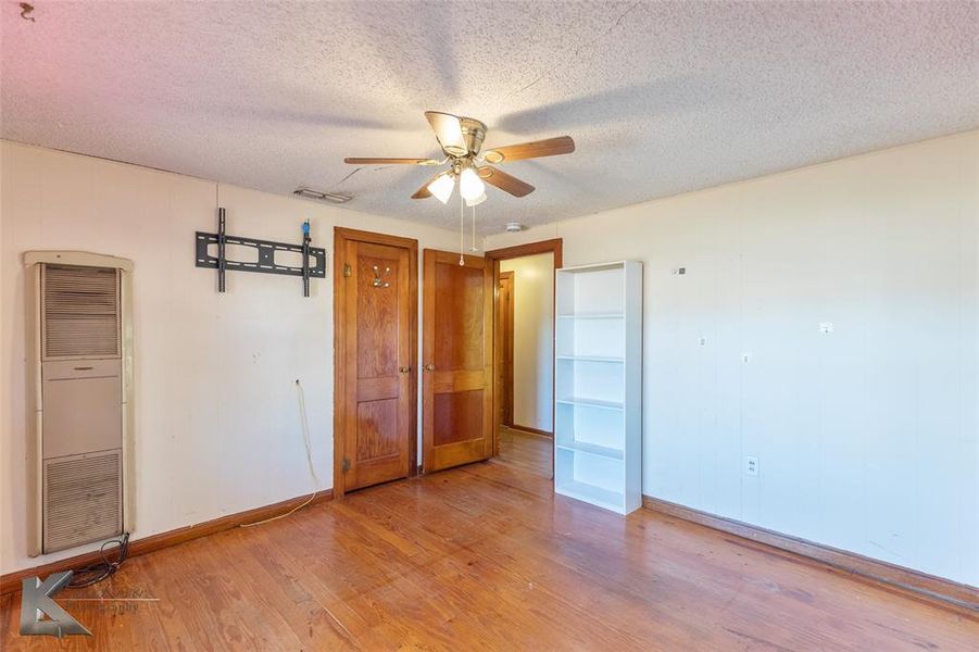 Unfurnished bedroom with a heating unit, light wood-style floors, a textured ceiling, and a ceiling fan Unfurnished bedroom with a heating unit, light wood-style floors, a textured ceiling, and a ceiling fan