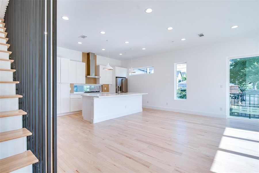 Kitchen with high end fridge, wall chimney exhaust hood, light hardwood / wood-style flooring, hanging light fixtures, and white cabinetry