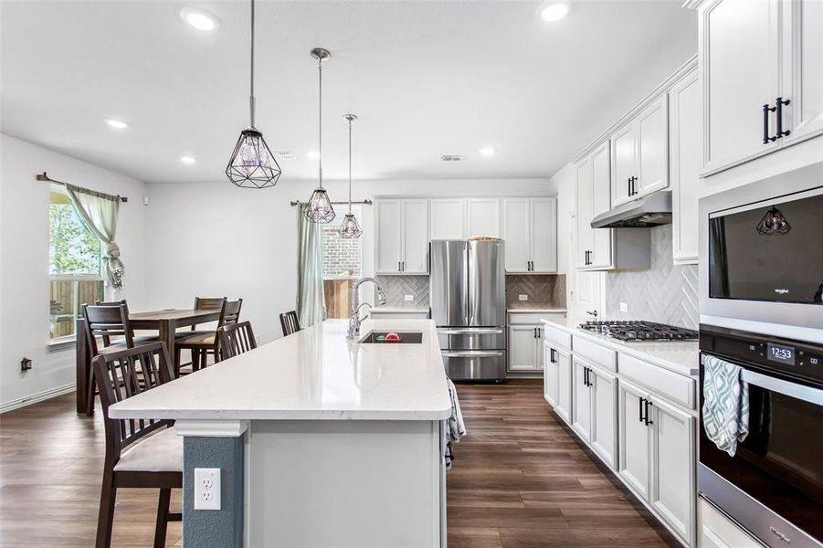 Kitchen with stainless steel appliances, under cabinet range hood, recessed lighting, tasteful backsplash, and dark wood-style flooring