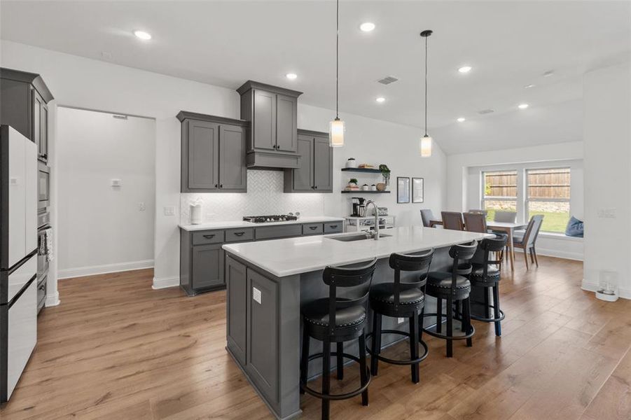 Kitchen with gray cabinetry, a kitchen breakfast bar, backsplash, decorative light fixtures, and light wood-style flooring