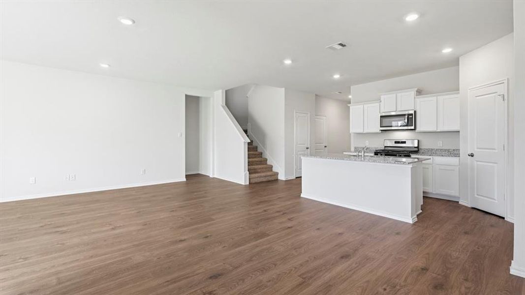 Kitchen featuring white cabinetry, an island with sink, appliances with stainless steel finishes, open floor plan, and dark wood-type flooring