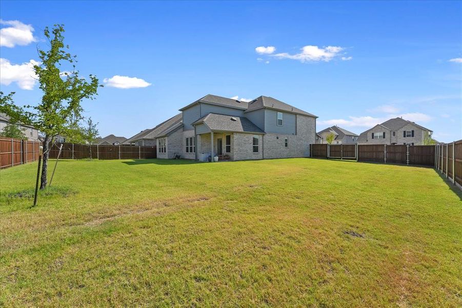 Expansive backyard featuring a large green lawn, wood privacy fencing, and a covered patio area