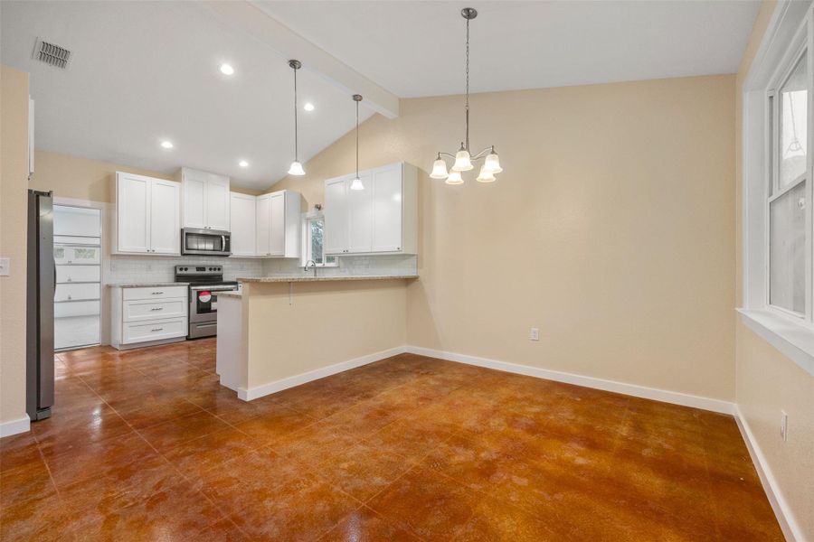 Kitchen featuring white cabinetry, a breakfast bar, a peninsula, hanging light fixtures, and stainless steel appliances