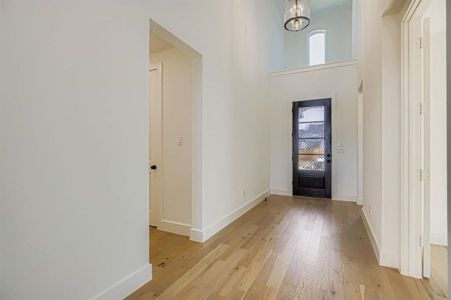 Foyer featuring plenty of natural light, light wood-style floors, a towering ceiling, and a chandelier Foyer featuring plenty of natural light, light wood-style floors, a towering ceiling, and a chandelier
