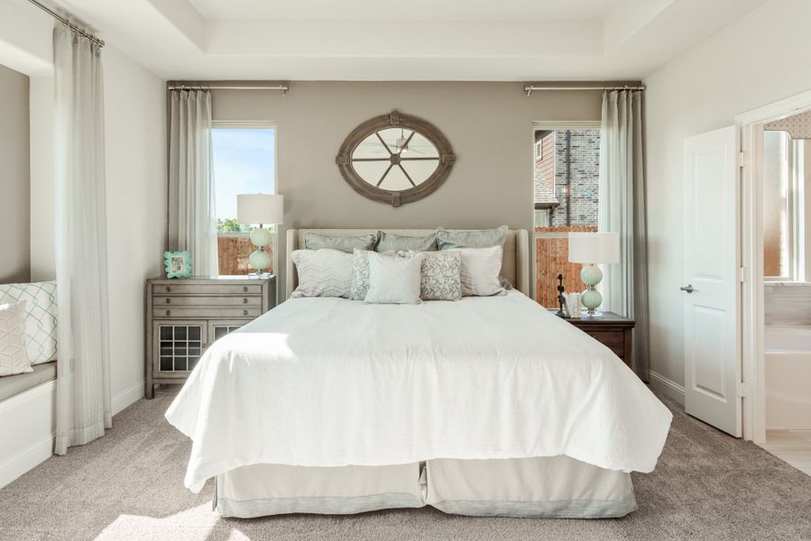Master bedroom with king bed, neutral carpet, two windows, and decorative oval mirror above headboard