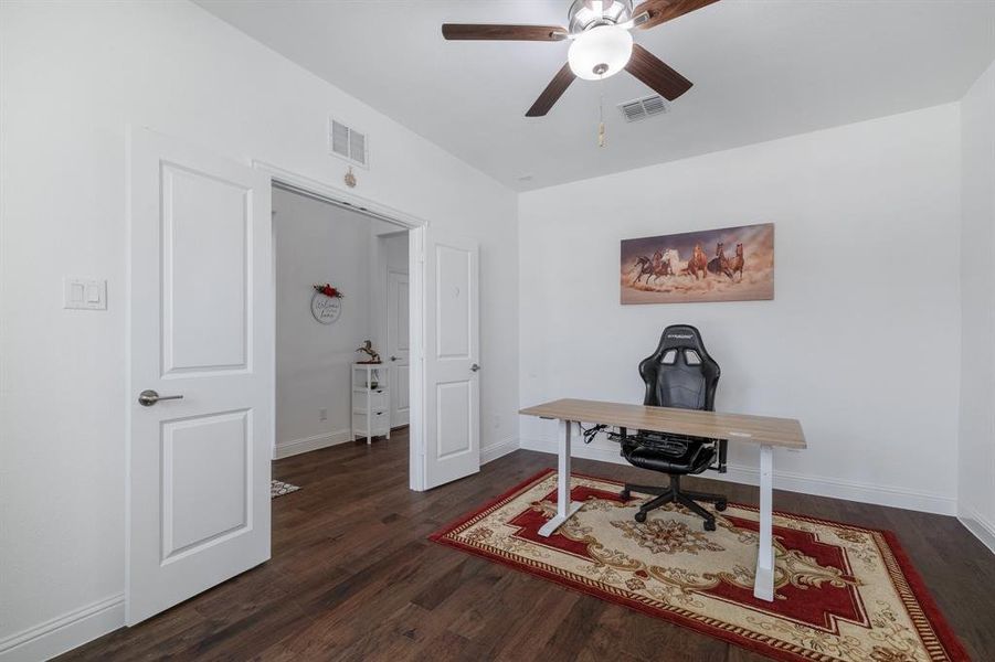 Home office with ceiling fan, wood finished floors, visible vents, and baseboards