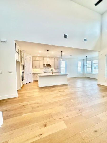 A well-lit open floor plan integrates a pristine kitchen and living area, featuring high ceilings and light hardwood flooring.