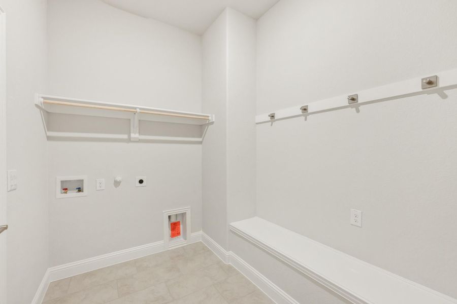 Laundry room with white walls, upper shelving, built-in bench, and washer and dryer hookups on tile floor Laundry room with white walls, upper shelving, built-in bench, and washer and dryer hookups on tile floor