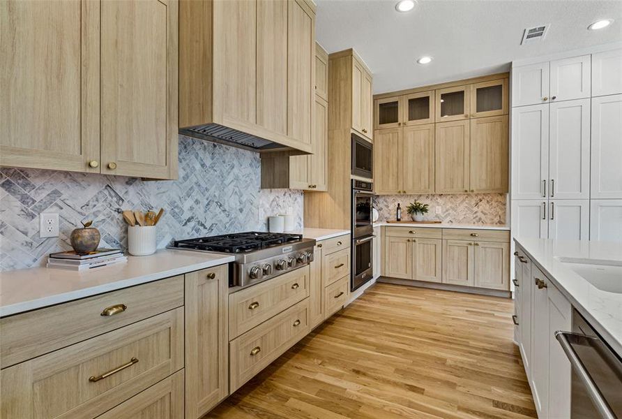 Kitchen with custom exhaust hood, light brown cabinets, decorative backsplash, appliances with stainless steel finishes, and light hardwood / wood-style flooring