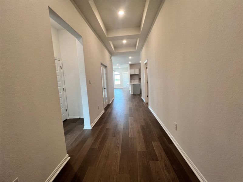 Corridor with dark wood-style flooring, a textured wall, a raised ceiling, and recessed lighting Corridor with dark wood-style flooring, a textured wall, a raised ceiling, and recessed lighting