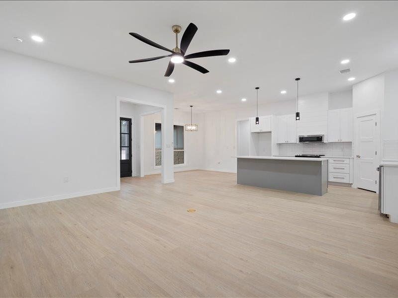 Spacious open-concept living area featuring light wood flooring, white walls, and recessed lighting