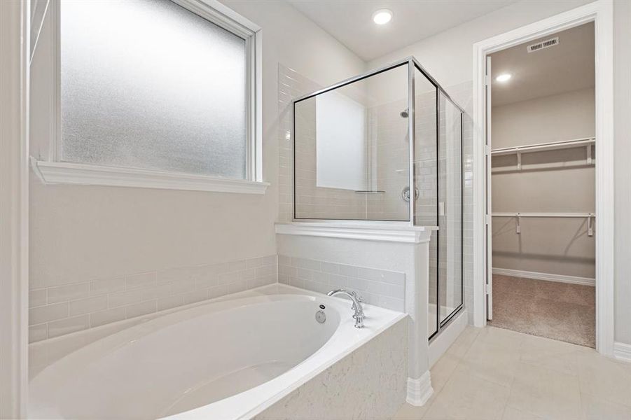 This additional view of your primary bathroom features tile flooring, fresh paint, walk-in shower, a separate garden tub, and a large walk-in closet.