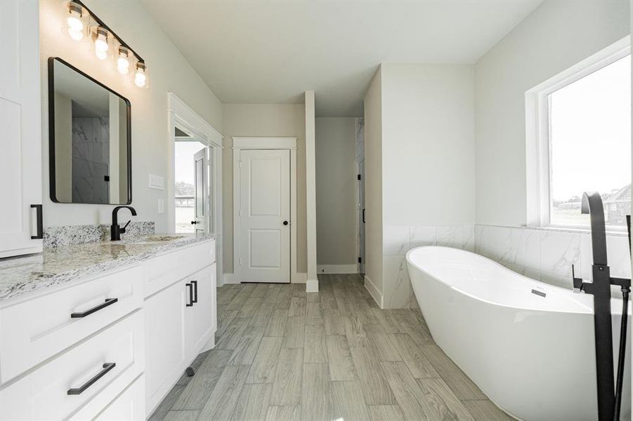 Primary bath featuring dual sink vanity, a stand-alone tub, wood tiled floors, and plenty of natural light. Primary bath featuring dual sink vanity, a stand-alone tub, wood tiled floors, and plenty of natural light.