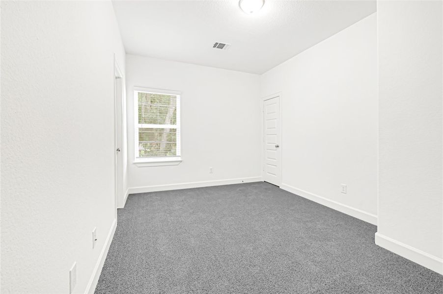 This photo shows a bright, unfurnished room with clean white walls and a gray carpet. It features a window for natural light and a simple ceiling light fixture. There are two doors, adding functionality to the space. This photo shows a bright, unfurnished room with clean white walls and a gray carpet. It features a window for natural light and a simple ceiling light fixture. There are two doors, adding functionality to the space.